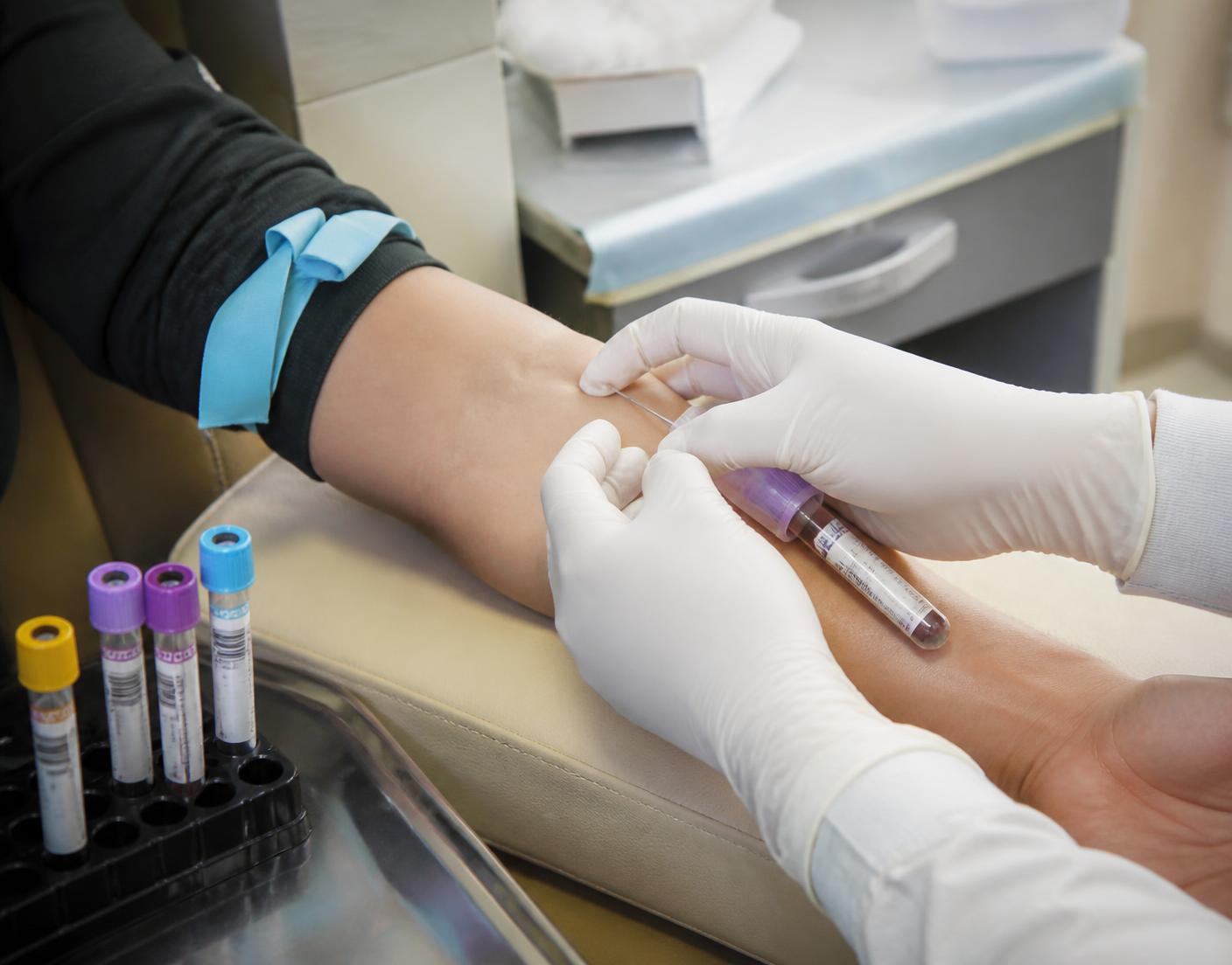 Gloved hands performing a venipuncture blood draw with collection tubes